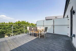 Ein Balkon mit Glastrennwand, einem Tisch und Stühlen sowie Blick auf grüne Bäume.