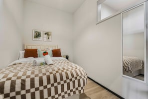 A hotel room with a checkered bedspread, a mirror, and two framed pictures on the wall. - 3-Bed Barry Island Apartment | Stunning Sea Views (Barry)