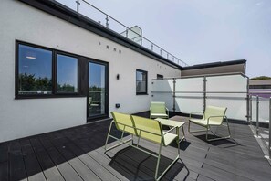 A rooftop terrace with a wooden deck, two chairs, and a table. - 3-Bed Barry Island Apartment | Stunning Sea Views (Barry)