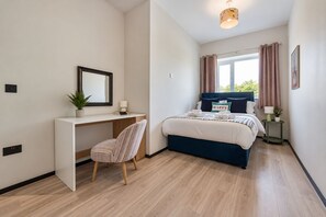 Een moderne slaapkamer met een bed, bureau, stoel en een raam met gordijnen.