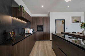 A modern kitchen with dark wood cabinetry, a black countertop, and a built-in oven. - 3-Bed Barry Island Apartment | Stunning Sea Views (Barry)