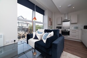 Ett modernt vardagsrum med en soffa, ett soffbord i glas och utsikt över en historisk byggnad.