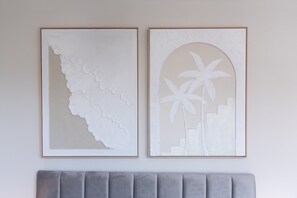 Zwei gerahmte Kunstwerke an einer Wand über einem grau gepolsterten Kopfteil.