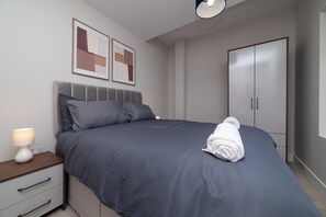 A neatly made bed with a grey duvet, a bedside table with a lamp, and a wardrobe with two doors. - Chic Old Town Apartment | Free Parking (Kingston upon Hull)