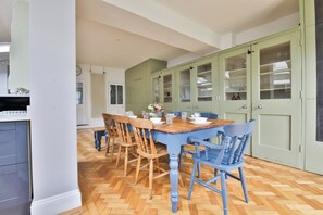 A dining area with a wooden table and chairs, a kitchen with green cabinets, and a herringbone-patterned floor. - Elegant Victorian Home with Pool Table & Parking (Cardiff)