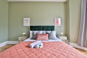 A neatly made bed with a pink quilt, two bedside tables with lamps, and two framed artworks on the wall. - Elegant Victorian Home with Pool Table & Parking (Cardiff)