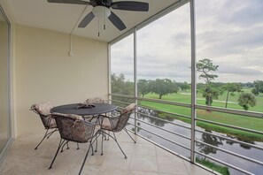 Ein Balkon mit Tisch und Stühlen, einem Deckenventilator und Blick auf einen Park mit einem See.