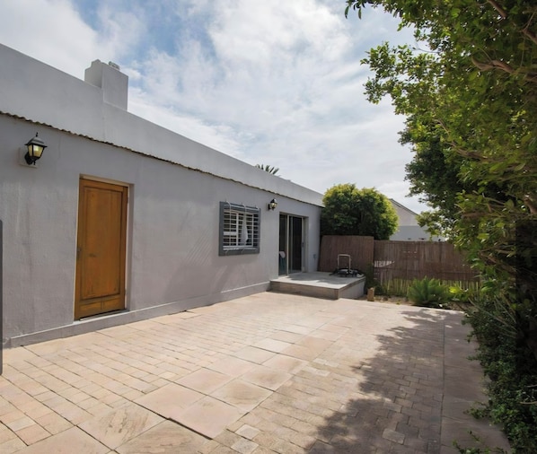 Un edificio residencial con un patio empedrado, una puerta de madera y un pequeño jardín.