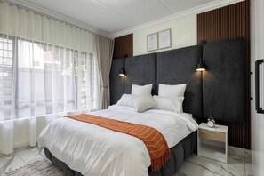 A modern bedroom with a large bed, a bedside table, and a nightstand. - Elegant 2-Bedroom Retreat in Fourways, Johannesburg (Sandton)