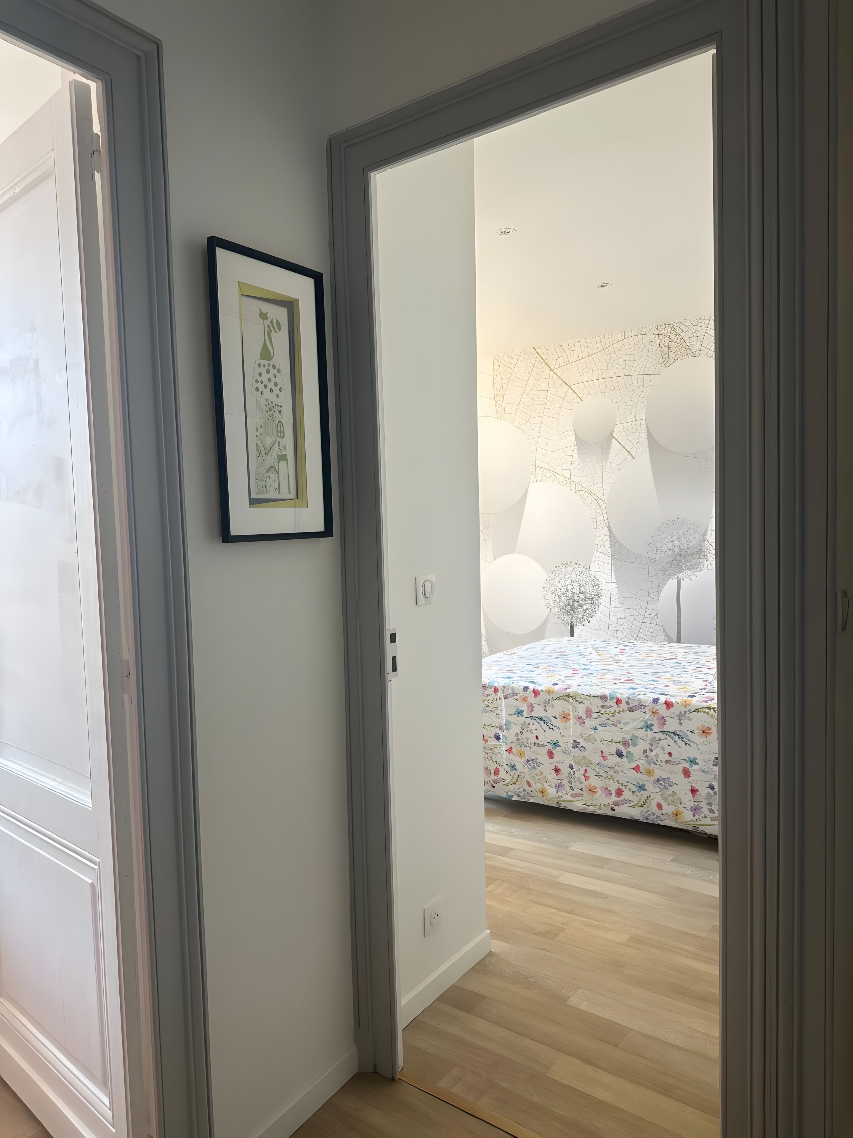 A hallway leading to a bedroom with a floral bedspread, a framed picture on the wall, and a ceiling with a geometric light fixture.