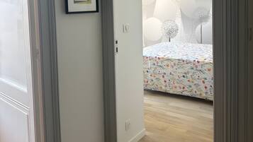 A hallway leading to a bedroom with a floral bedspread, a framed picture on the wall, and a ceiling with a geometric light fixture.