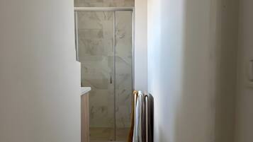 A narrow hallway leading to a bathroom with a glass shower enclosure and a towel rack with multiple towels.