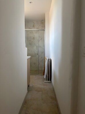Un pasillo estrecho que conduce a un baño con cabina de ducha de vidrio y un perchero con varias toallas.