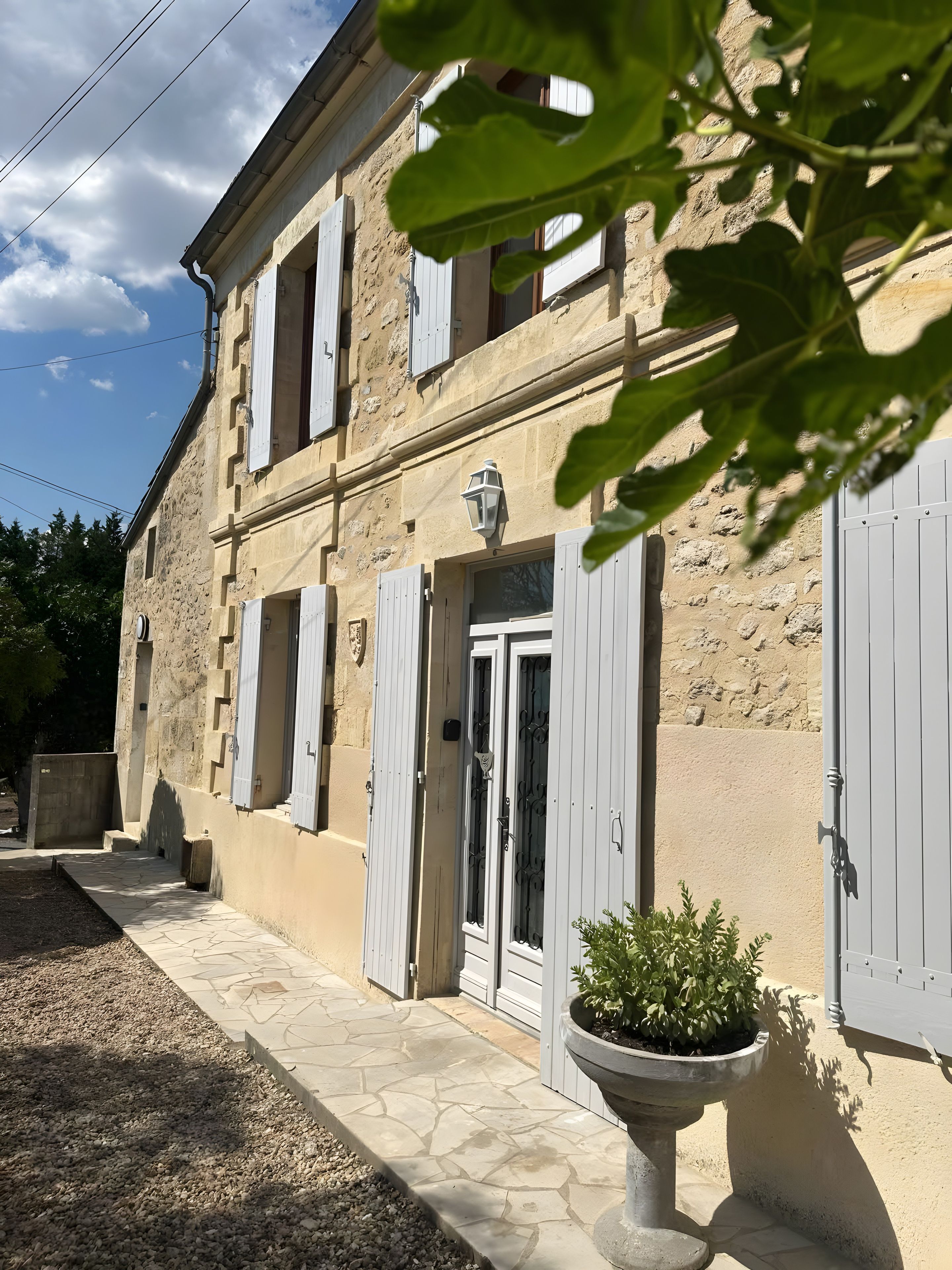 A stone building with white shutters, a potted plant, and a stone pathway.