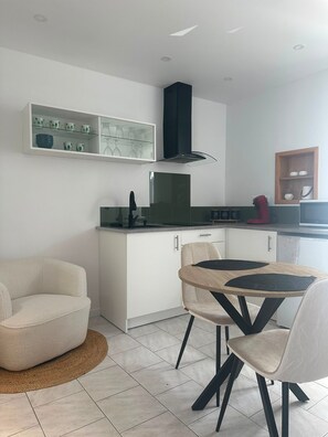 A modern kitchen with white cabinetry, a black range hood, and a dining area with a round table and chairs.
