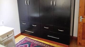 Una habitación con un armario negro grande, una mesita de noche blanca y una alfombra estampada en el suelo.