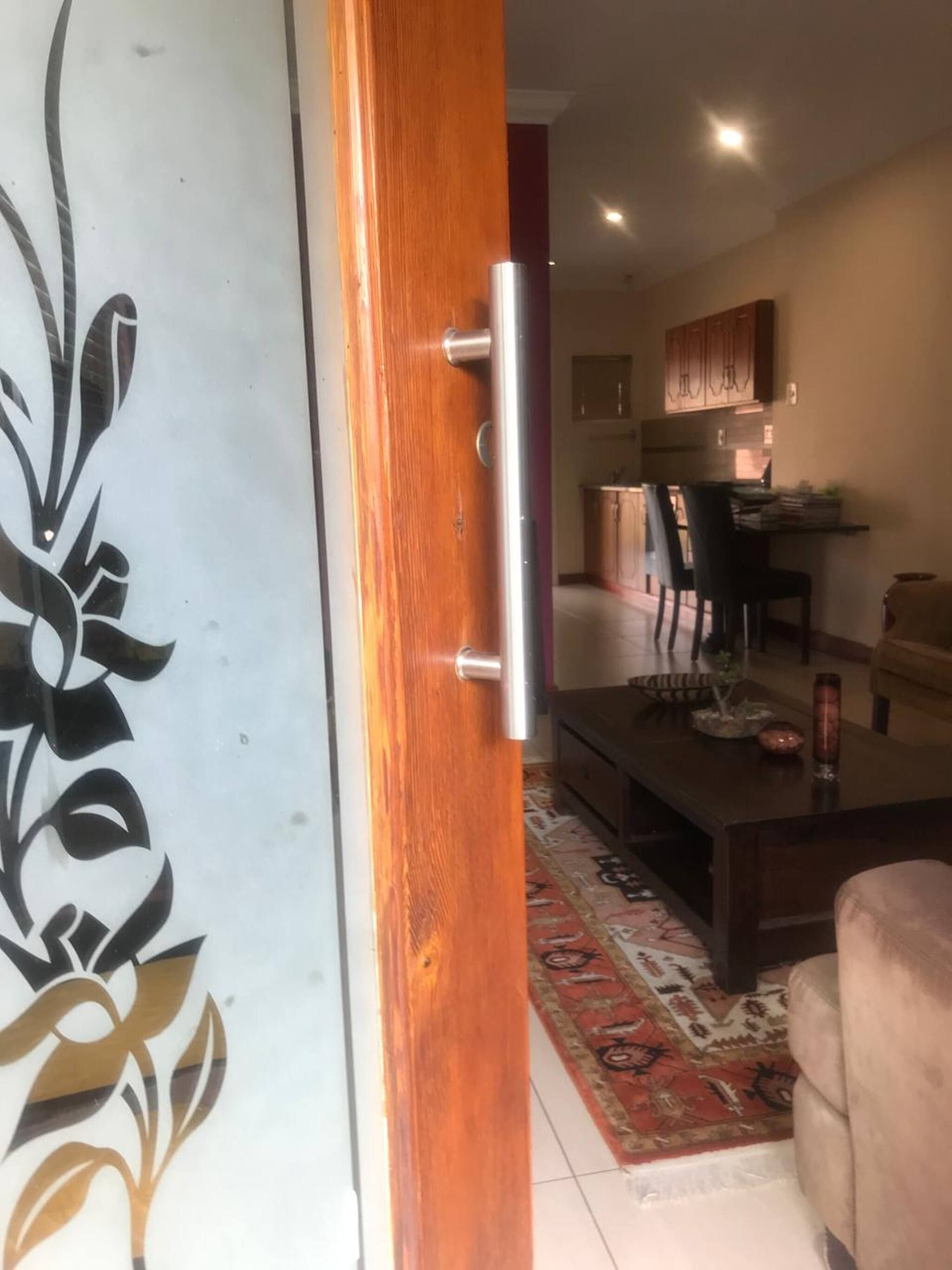 Un interior amb una porta de fusta, una zona de menjador amb caires, una taula i una cuina al fons.