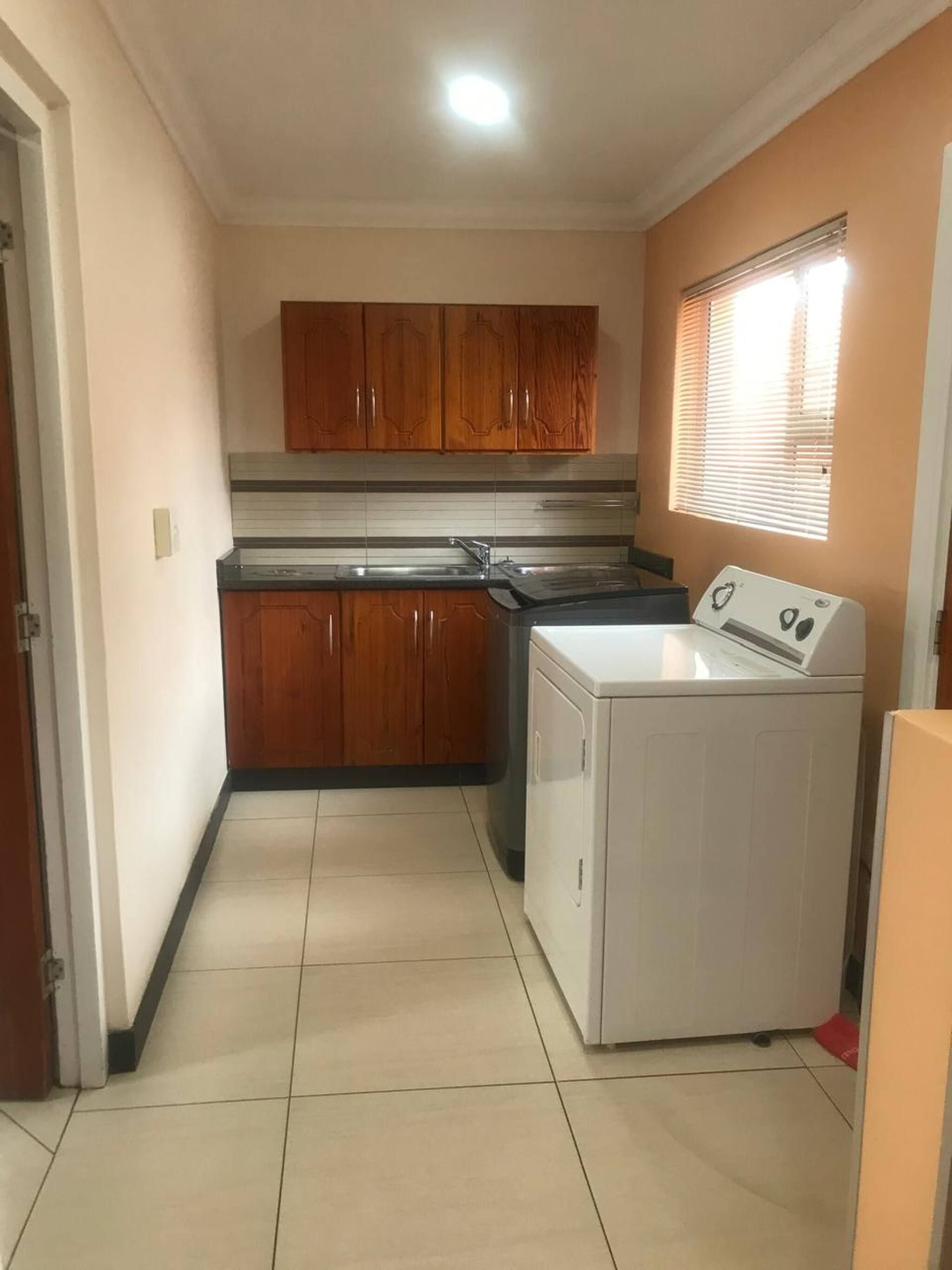 Una cocina compacta con armarios de madera, lavadora y ventana con persianas.