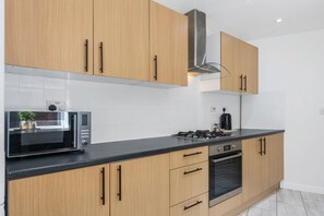 Een moderne keuken met houten kastjes, een roestvrijstalen afzuigkap, een magnetron, een waterkoker en een inbouwoven.