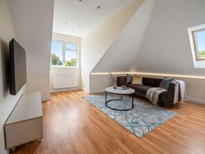 Ein modernes Wohnzimmer mit schrägverdachter Decke, einem Flachbildfernseher, einer Couch, einem Couchtisch und einem Fenster.