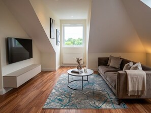 A modern living room with a flat-screen TV, a sofa, a coffee table, and a large window. - St Peters Nest -Stylish 1-Bed Flat (Croydon)