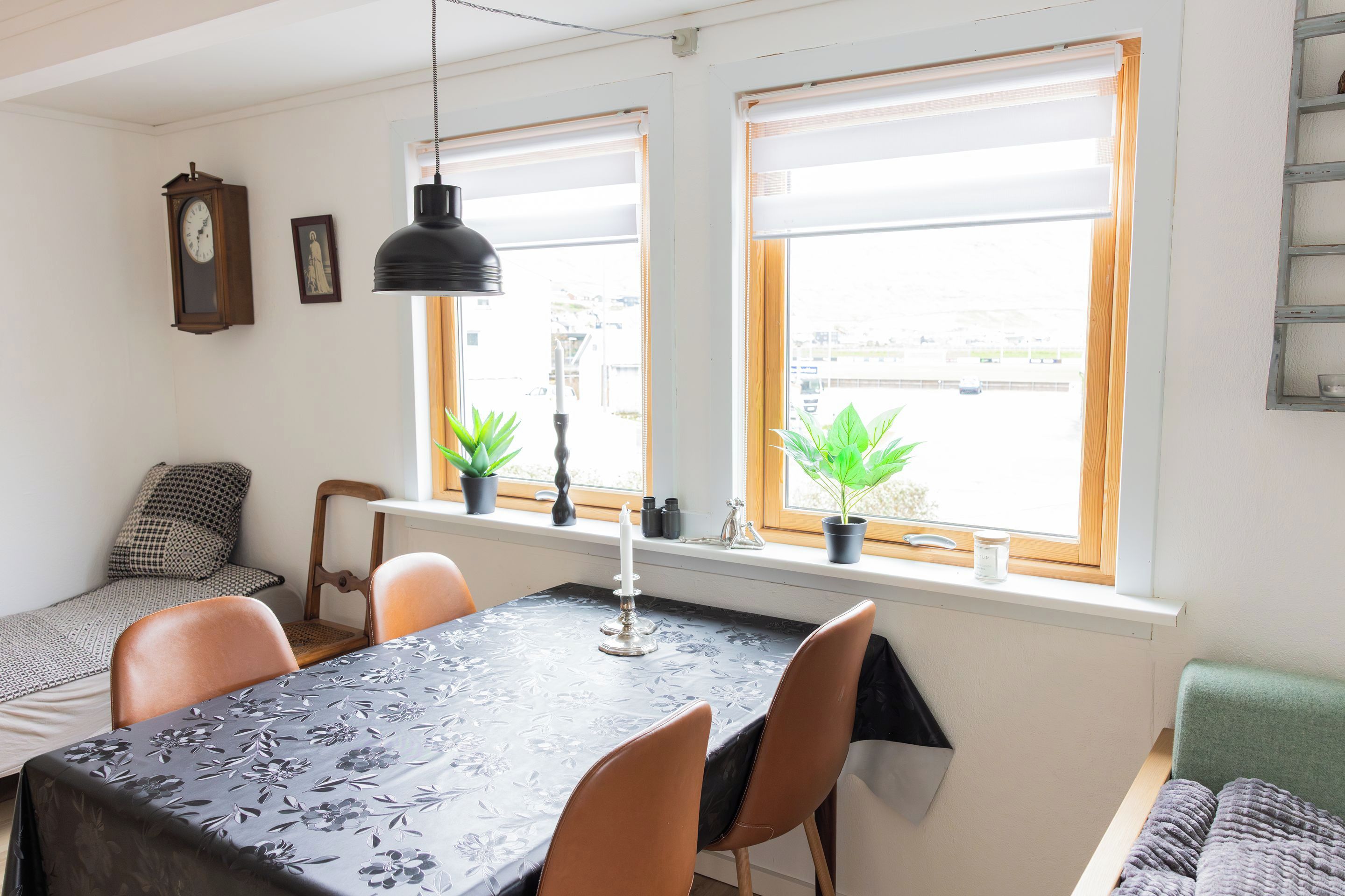 Un comedor con una mesa, sillas, un reloj y dos ventanas con plantas.