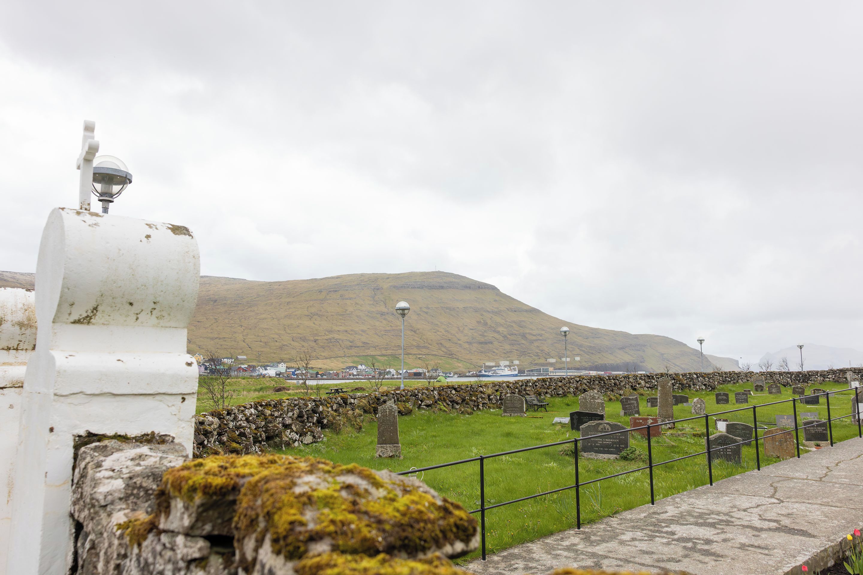 Un cementerio con lápidas, un muro de piedra y una montaña al fondo.