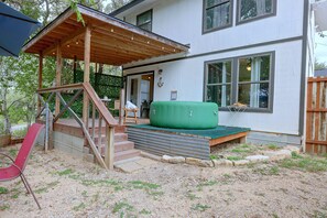 Kaksikerroksinen talo, jossa on katettu kuisti, vihreä ulkotila oleskelua varten ja punainen tuoli.