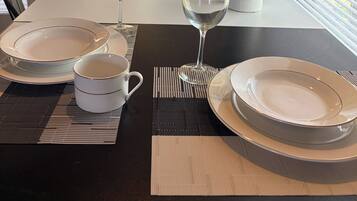 A dining table set with plates, a wine glass, and a cup, with a potted plant and a view of the outdoors.