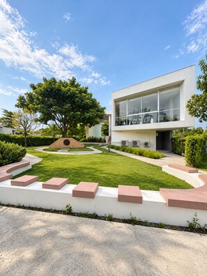 Une maison moderne avec une pelouse bien entretenue, un grand arbre et un ciel dégagé.
