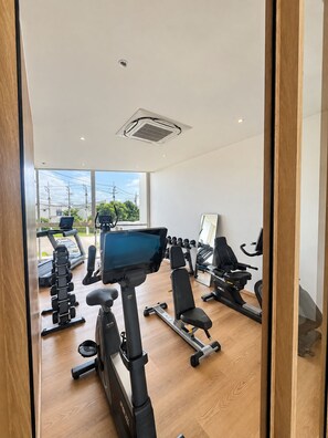 Un gimnasio moderno con diverso equipo de ejercicio, ventanas amplias y vistas al exterior.