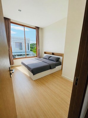 Une chambre moderne avec un grand lit, un plancher en bois et une vue sur un immeuble par la fenêtre.