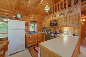 A cabin interior with wooden walls, a kitchen area including a refrigerator, stove, and microwave, and a dining area with a table and chairs. - Beach Days, Campfire Nights! Sturgeon Bay Getaway (Harbor Springs)