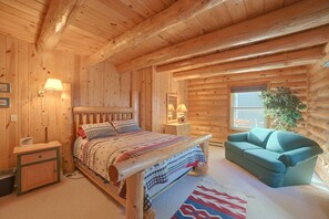 Un dormitori de cabana de fusta amb un llit, taules de nit, una commode, una cadira i una finestra.