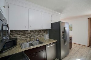 A kitchen with white cabinets, a stainless steel refrigerator, a microwave, and a sink with a faucet. - Small Town Charm: Historic Eastover Home (Eastover)