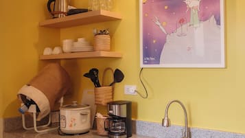 Une cuisine dotée d’un plan de travail en granit, d’un évier en acier inoxydable, d’une bouilloire, d’un grille-pain et d’une affiche du « Petit Prince » accrochée au mur.