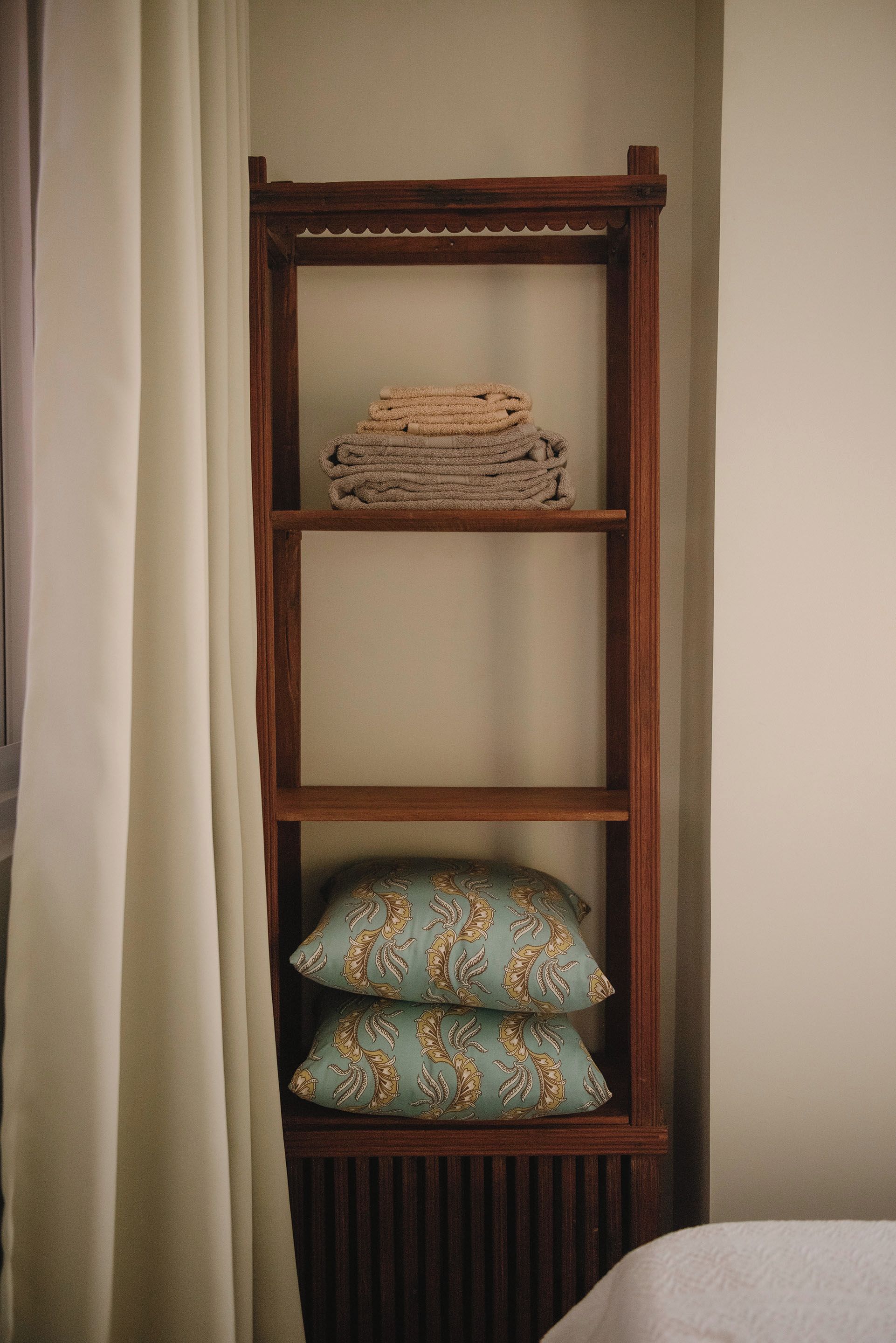 A wooden shelf unit with folded towels and patterned pillows.