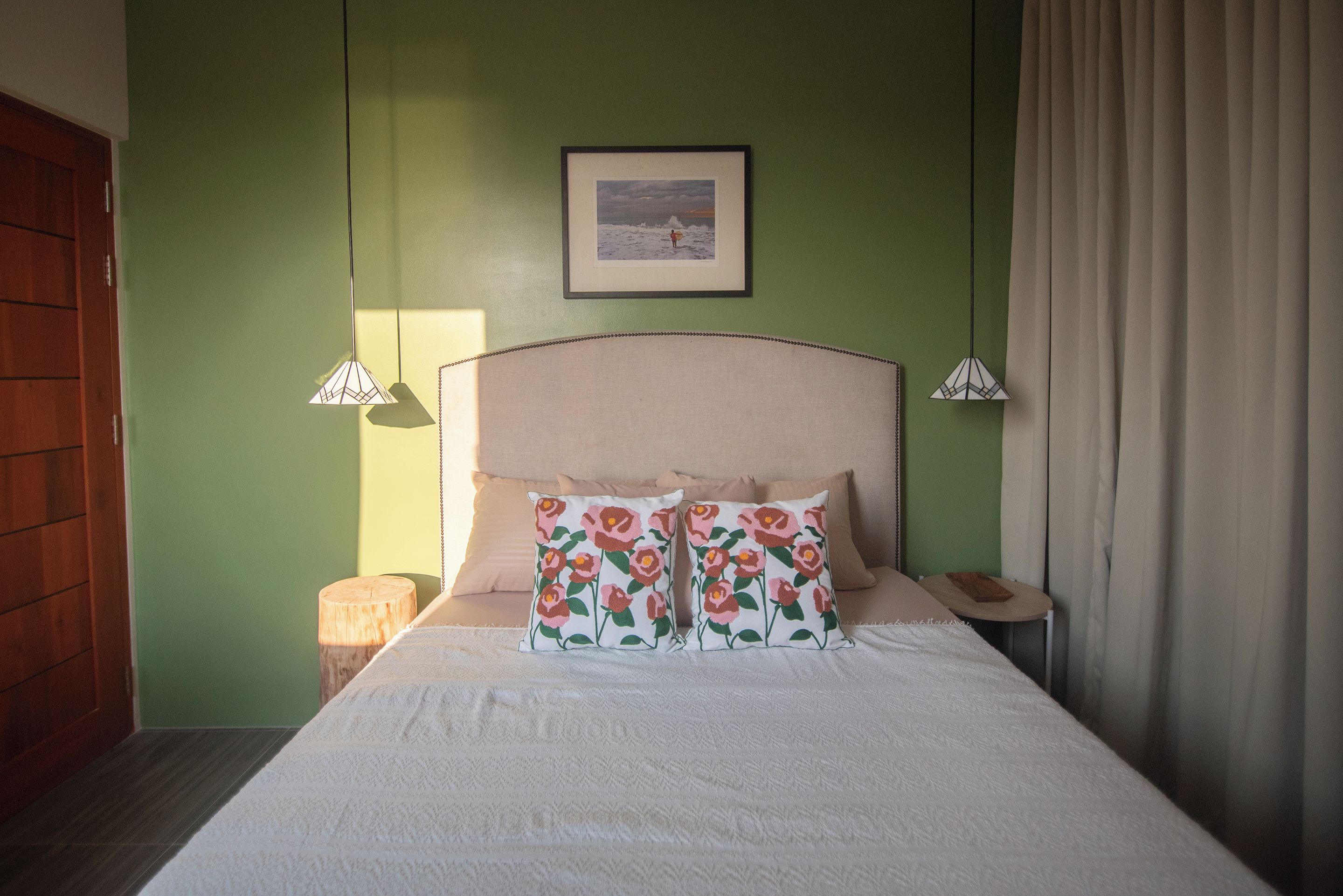 A bed with a headboard, two bedside lamps, a pillow with a floral pattern, and a framed picture on the wall.
