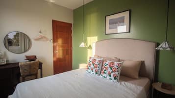 Une chambre à coucher avec un lit, une porte en bois, un miroir, un tableau encadré accroché au mur et une petite table avec une chaise.