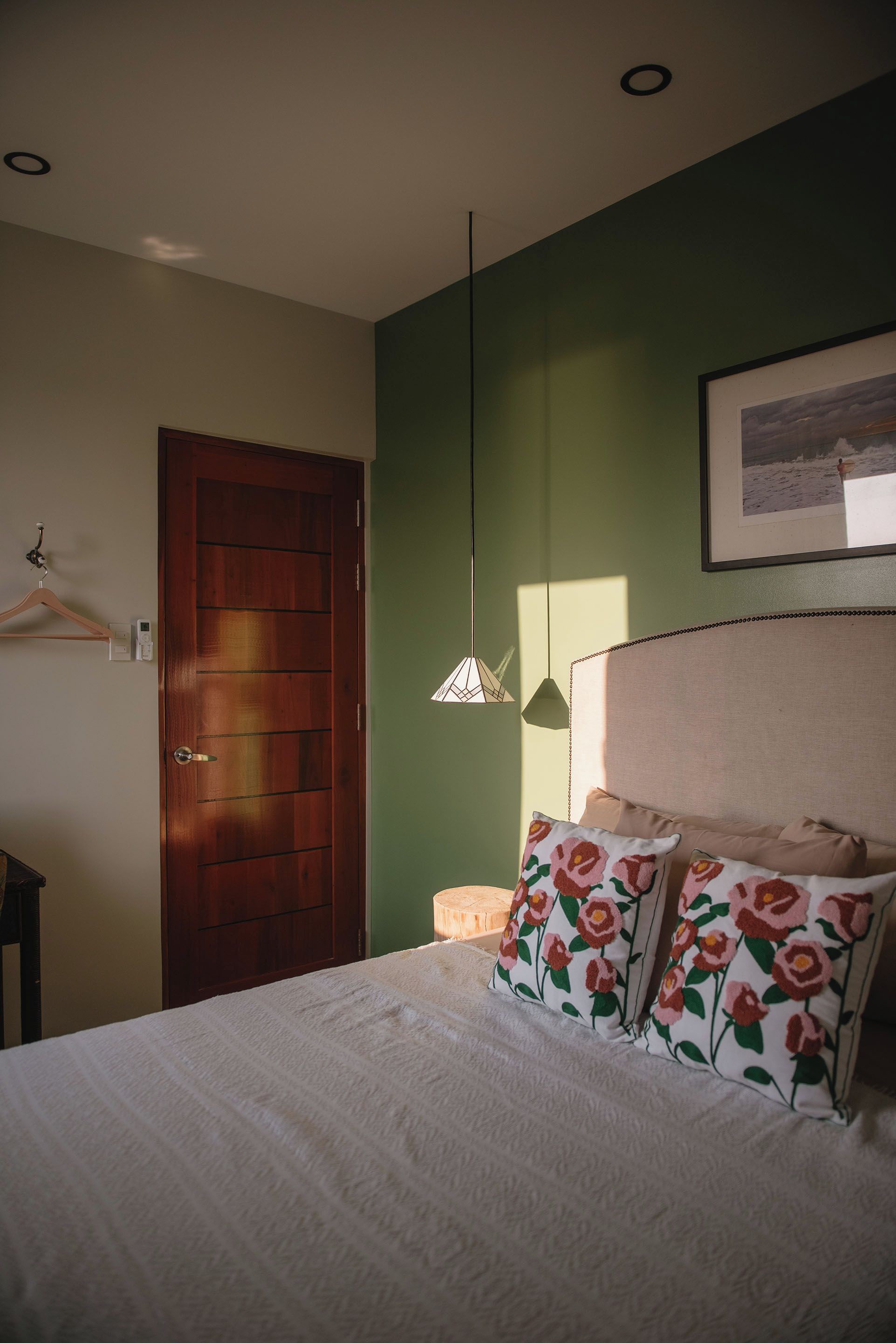 Un dormitorio con cama, una puerta de madera, una lámpara fijada a la pared y un cuadro enmarcado.