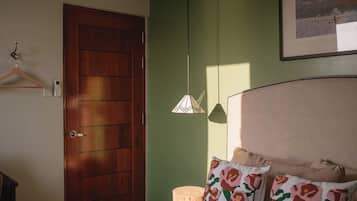 Un dormitorio con cama, una puerta de madera, una lámpara fijada a la pared y un cuadro enmarcado.