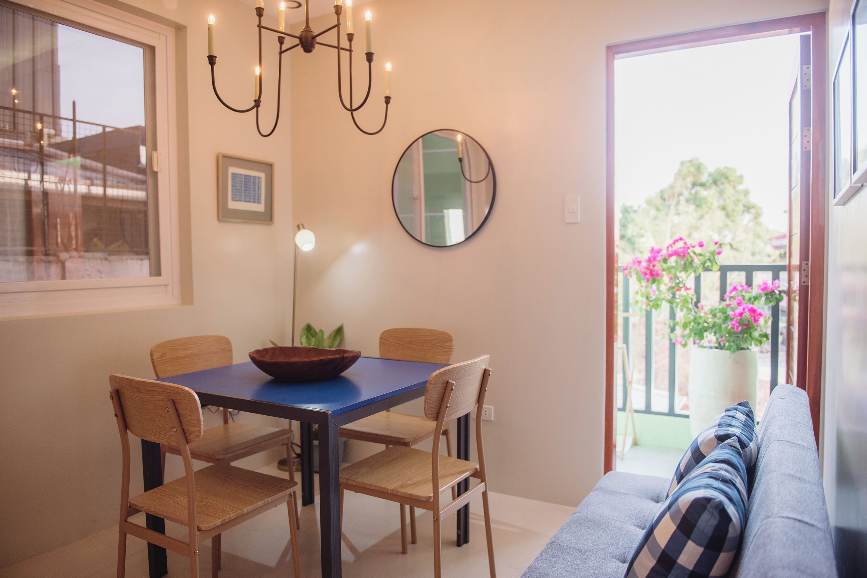 Un espace repas comprenant une table, des chaises, un lustre, un miroir et une vue sur un balcon orné de fleurs.