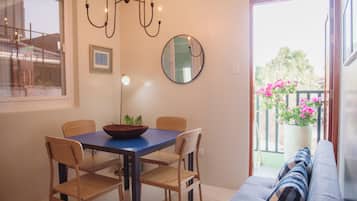 Un espace repas comprenant une table, des chaises, un lustre, un miroir et une vue sur un balcon orné de fleurs.