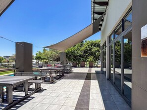 An outdoor patio area with tables and chairs, a pool, and a building with large windows. - Haus 189 Dainfern- Pool  Play Area Power Backup (Sandton)