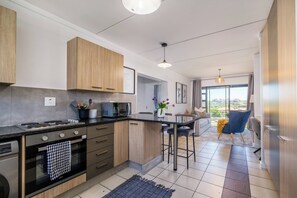 A modern kitchen with a central island, built-in appliances, and a dining area with a view. - Haus 189 Dainfern- Pool  Play Area Power Backup (Sandton)