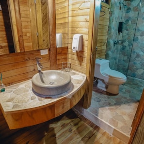 A bathroom with a wooden vanity, a stone sink, a mirror, a hand soap dispenser, a toilet, and a shower area with stone walls. - Hotel La Ardilla de Santa Fe (Santa Fe de Antioquia)