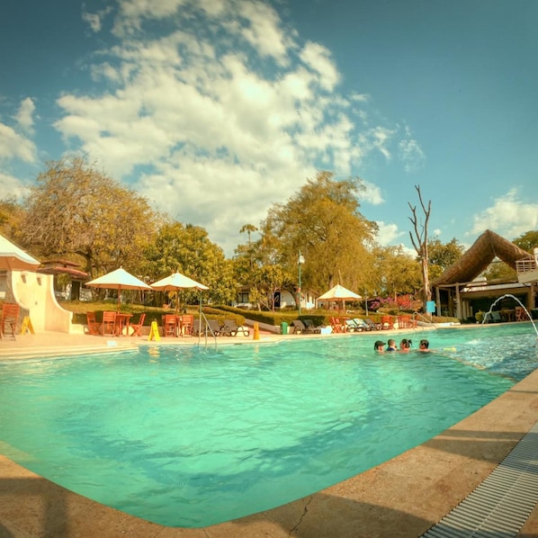 A swimming pool with lounge chairs and umbrellas, surrounded by trees and buildings. - Hotel La Ardilla de Santa Fe (Santa Fe de Antioquia)