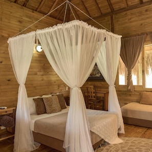 A wooden cabin room with a four-poster bed, a sofa, and a dining table. - Hotel La Ardilla de Santa Fe (Santa Fe de Antioquia)