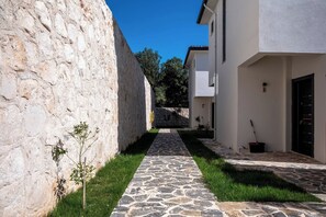 A narrow stone pathway leading to a building with a stone wall on one side and a white building on the other. - Villa Savaya-2 Antalya (Kaş)