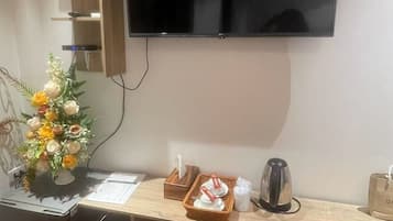 Ein Hotelzimmer mit einem flachbildfernseher an der Wand, einem Holztisch mit einem Korb mit Pflegeprodukten, einer kleinen Pflanze und einem Wasserkocher.